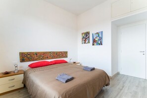 A bedroom with a bed, a nightstand, a drawer, a door, and two wall-mounted artworks. - GuestHost - Fully furnished apartment in modern style, can accommodate up to 6 people!Very close to the Cascine Park where you can walk, jog or ride a bike. Inside the park is the Visarno Arena (inside the Hippodrome), the area is a perfect show for grea (Firenze)