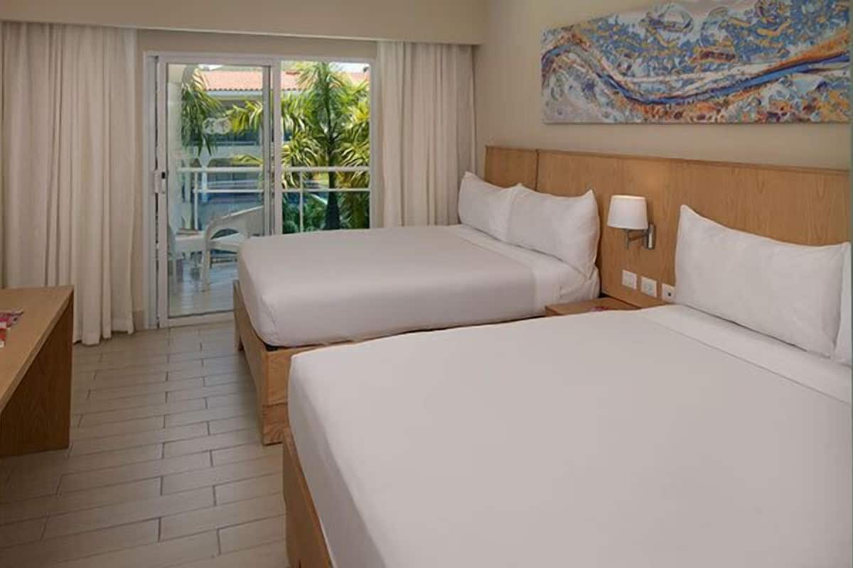 Ein Hotelzimmer mit zwei Betten, einem Schreibtisch, einem Fernseher und einem Balkon mit Vorhängen.