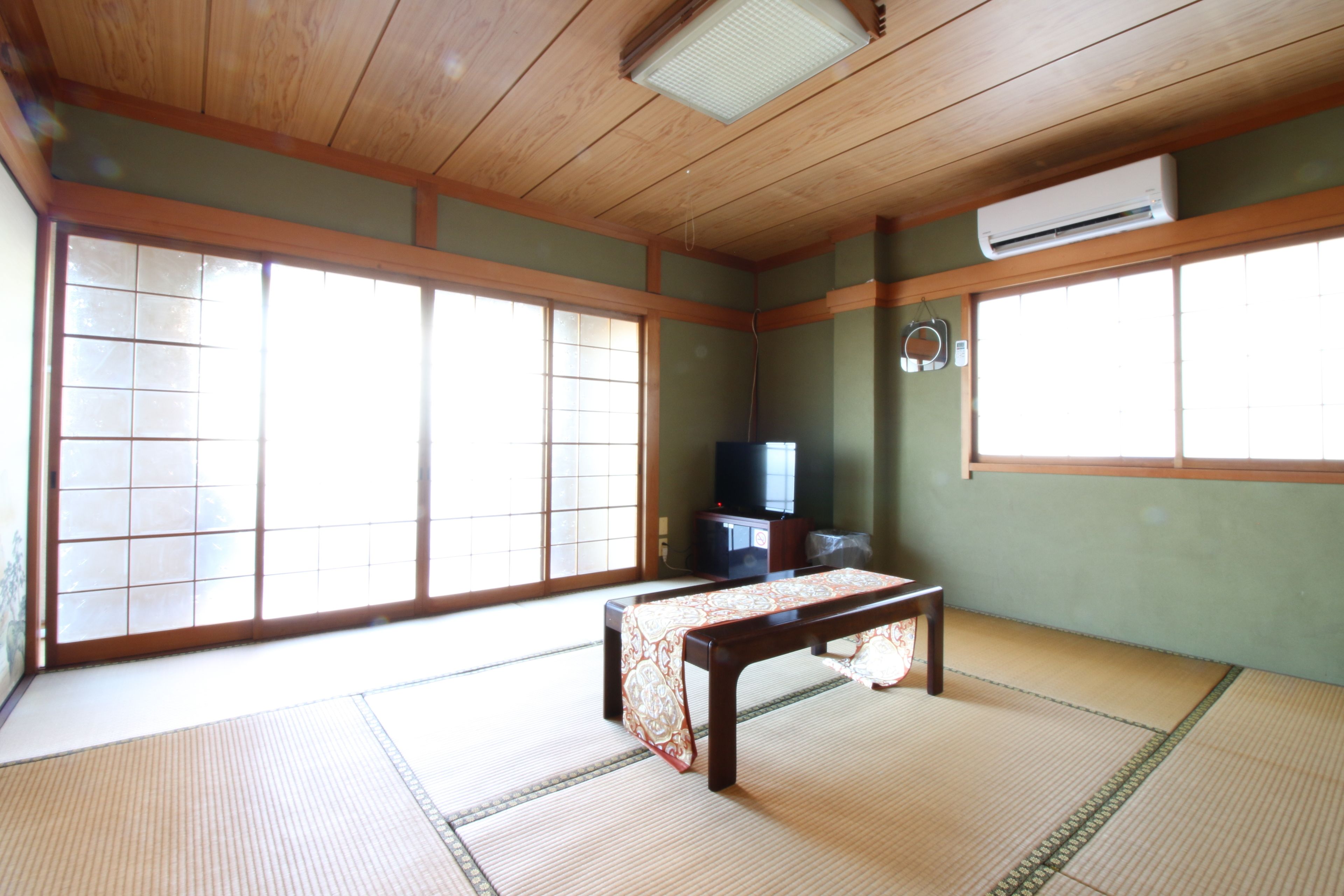 A traditional Japanese room with tatami flooring, a low wooden table, sliding doors, and a television.