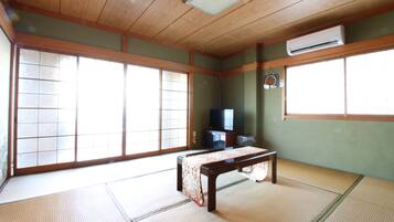 A traditional Japanese room with tatami flooring, a low wooden table, sliding doors, and a television.