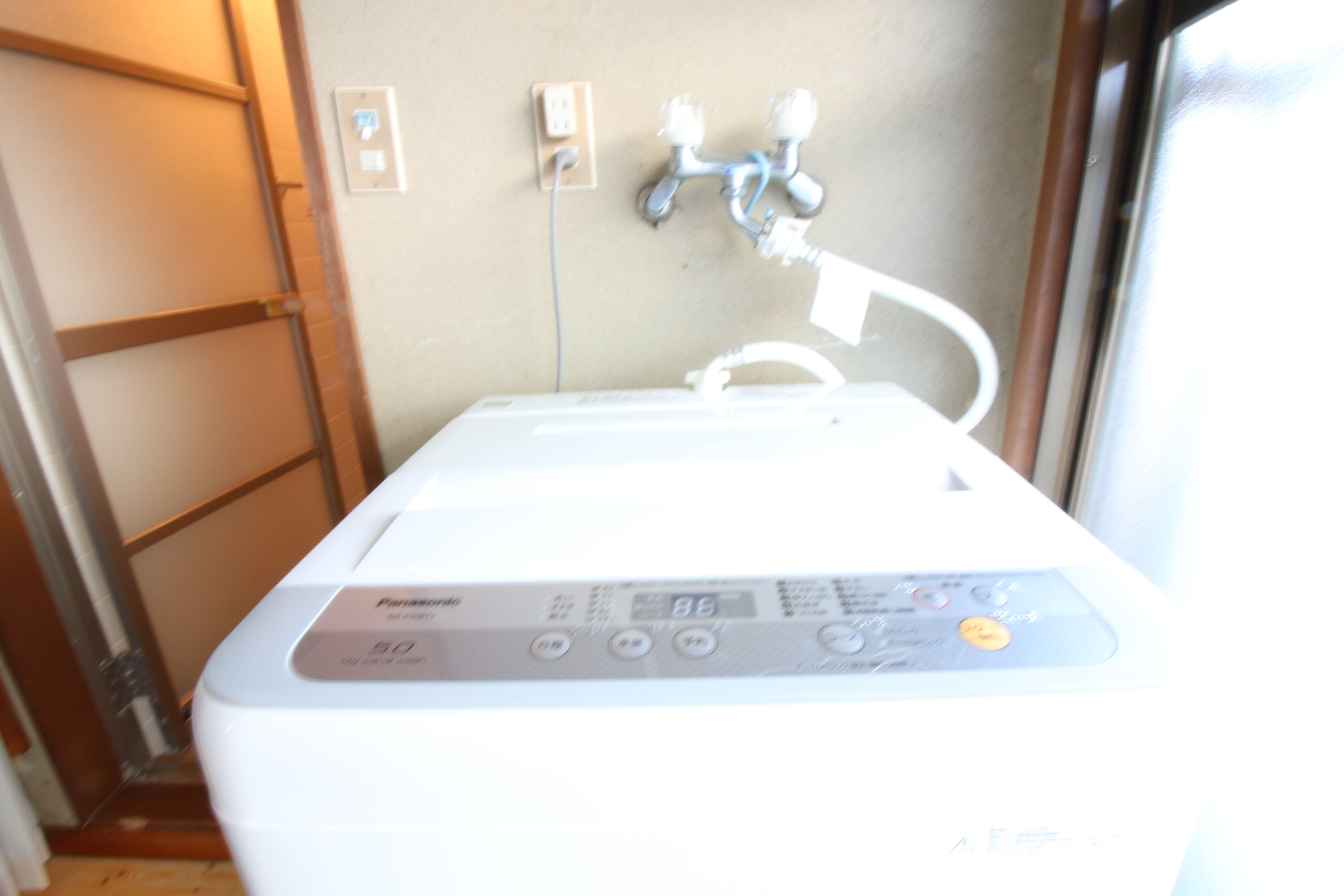A white Panasonic water heater with a digital display, connected to a wall-mounted plumbing system.