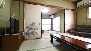 A traditional Japanese room with tatami flooring, a low wooden table, a sofa, and sliding doors with artwork. - Hikari No Yado (Anan)