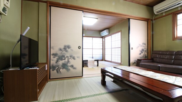 A traditional Japanese room with tatami flooring, a low wooden table, a sofa, and sliding doors with artwork. - Hikari No Yado (Anan)