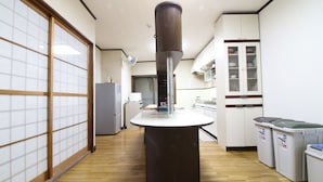 A kitchen with a central island, a refrigerator, cabinets, and a trash bin. - Hikari No Yado (Anan)