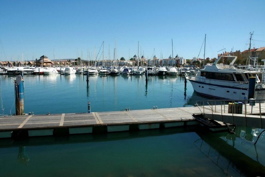 Un port de plaisance où sont amarrés de nombreux bateaux, avec un quai en bois et des bâtiments en arrière-plan.