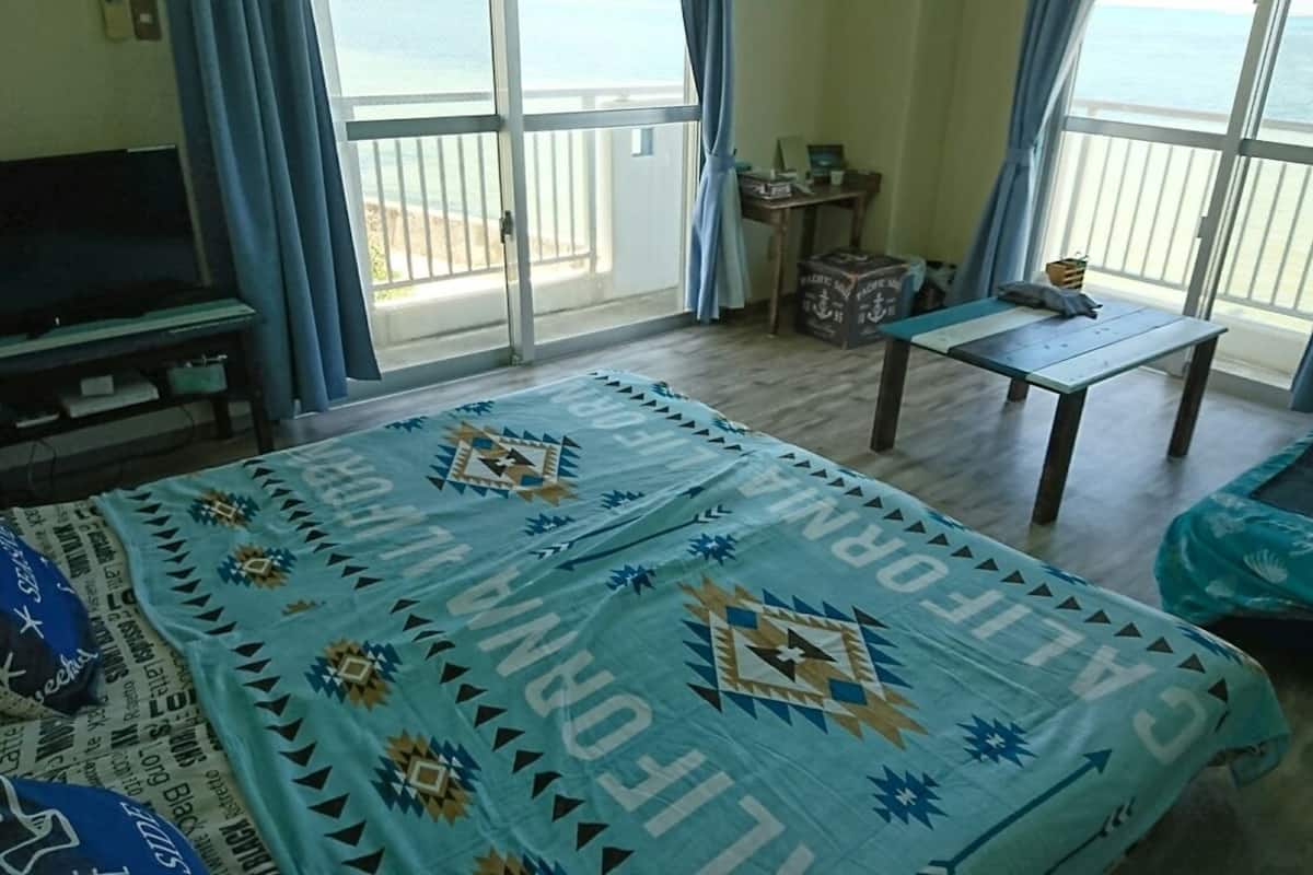 A room with a bed, a TV, a table, and a view of the sea.