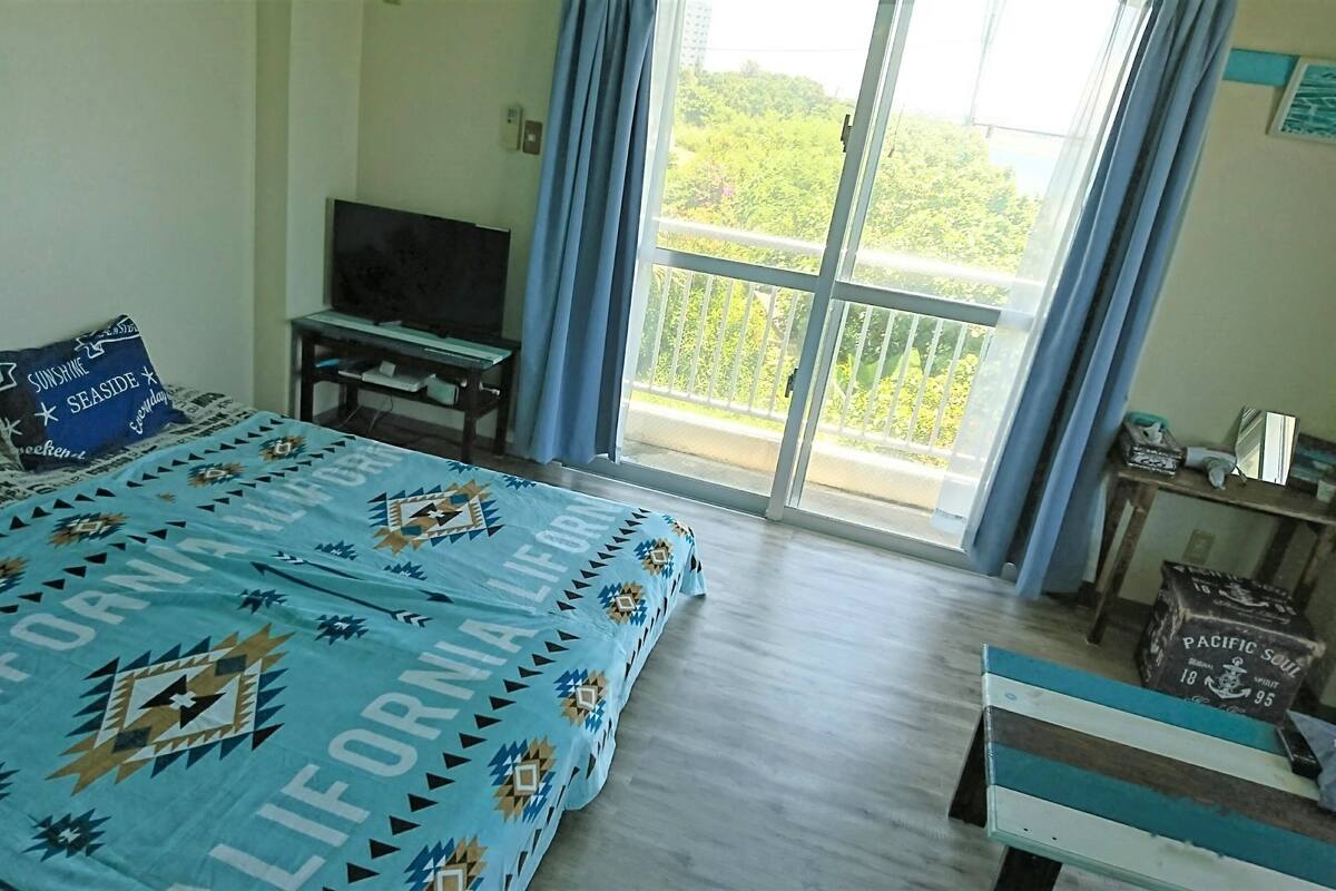 Ein Schlafzimmer mit Bett, Fernseher, Balkon und Blick sowie einem Tisch mit Gegenständen.