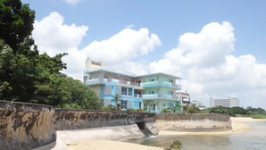 Una propiedad frente a la playa con un edificio de varios pisos, un muro de contención de concreto y una playa de arena.