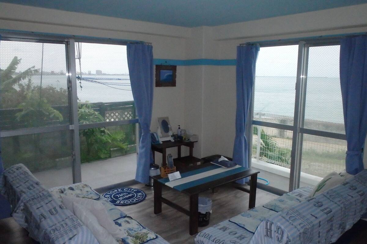 Ein Zimmer mit Meerblick, einem Tisch, zwei Sofas und einem kleinen Schreibtisch mit Stuhl.