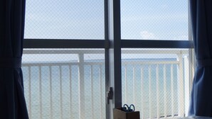 Habitación con vista al mar a través de una ventana con barandilla blanca. En una mesa junto a la ventana, hay una caja de madera pequeña con tijeras.