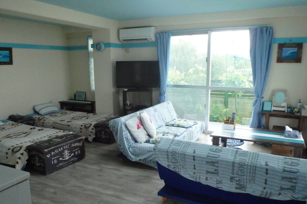 Ein Zimmer mit zwei Betten, einem Sofa, einem Fernseher und einem Fenster mit Vorhängen.
