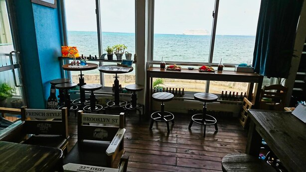 Un rincón acogedor con bar, muebles de madera, vista al mar y un barco a lo lejos.