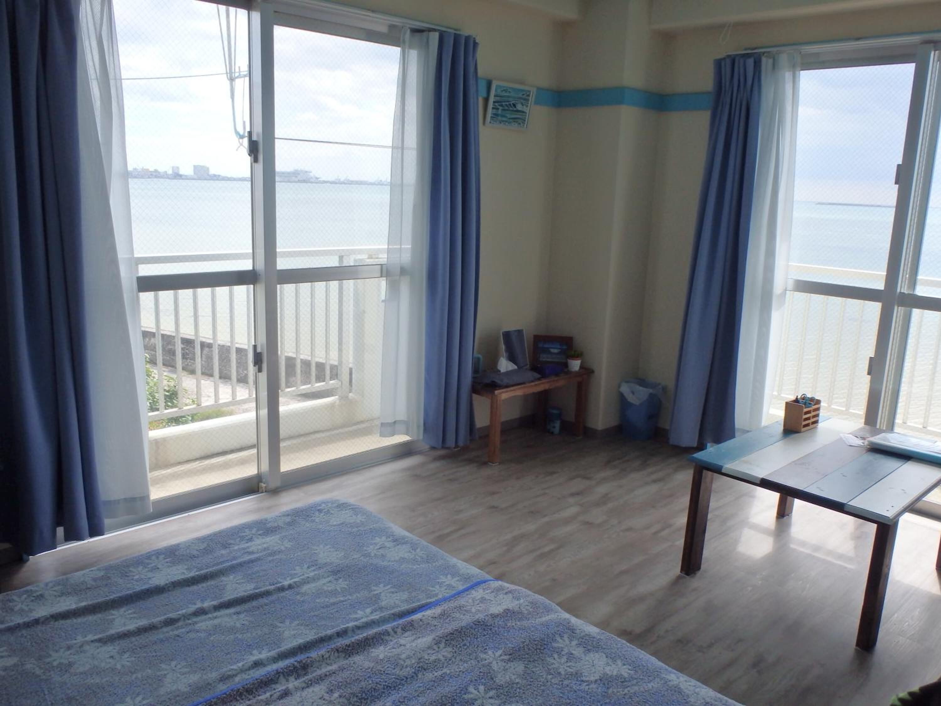 Une chambre avec un lit, une petite table et une vue sur la mer grâce à de grandes fenêtres.