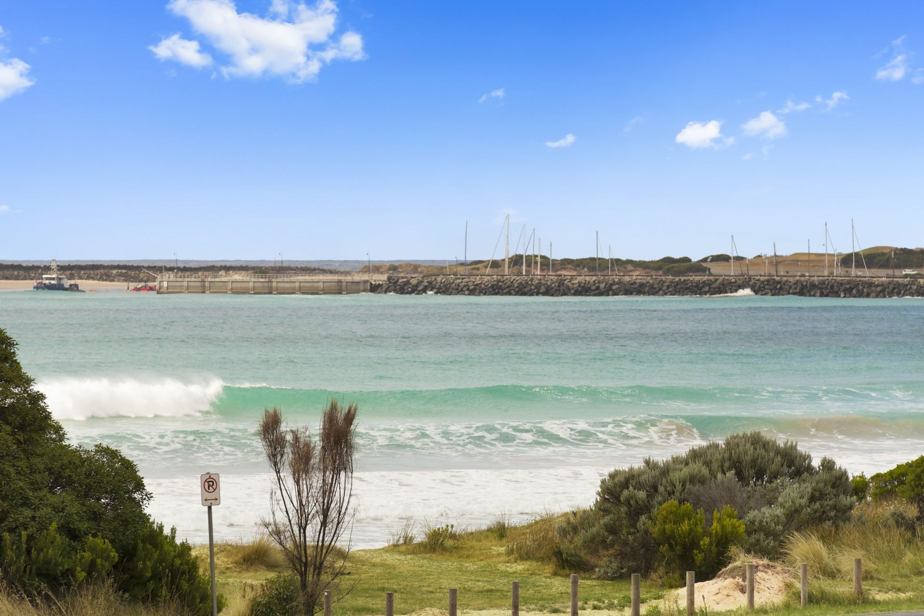 A coastal view with a clear sky, a sandy beach, and a rocky breakwater.