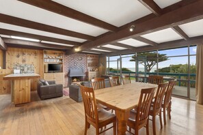A spacious room with a wooden dining table, chairs, a fireplace, and a large window overlooking a scenic view.