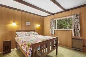 Une chambre à coucher avec un lit en bois, deux lampes fixées au mur, une fenêtre ornée de rideaux à motifs floraux et un radiateur.