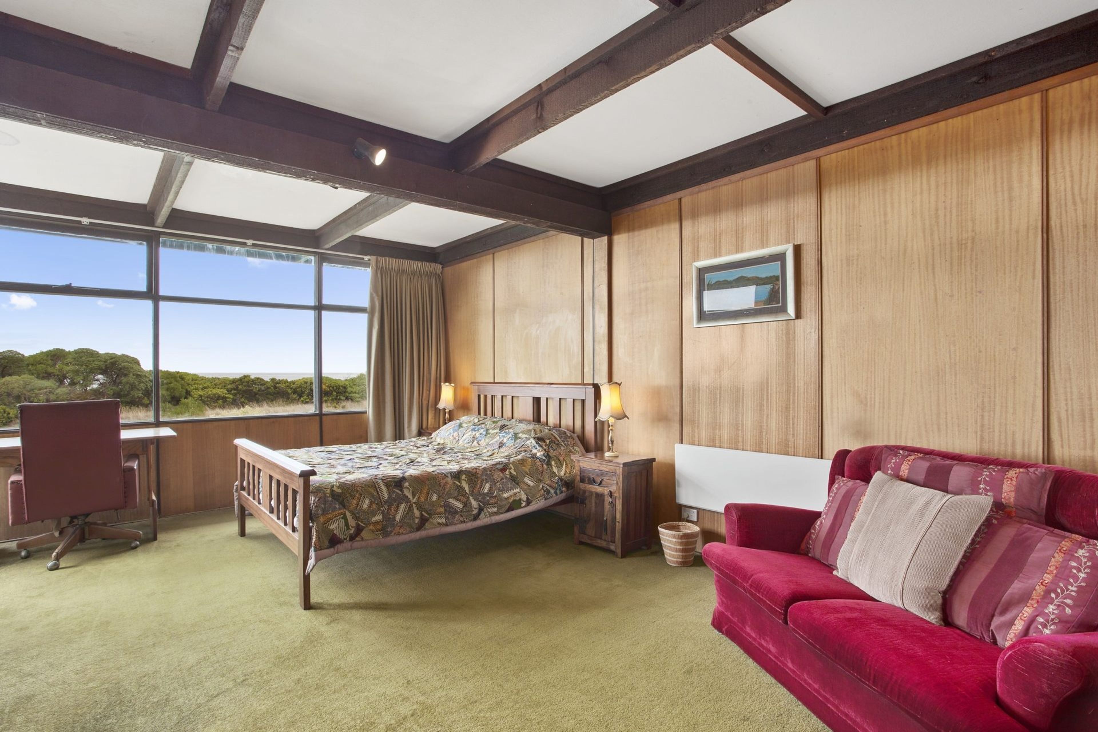 A bedroom with a bed, a red sofa, a desk, and a window with a view.