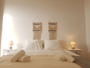A neatly made bed with white linens, two wall-mounted macramé wall hangings, and two bedside lamps on white nightstands. - Charming & Central Apartment in Traditional Chalet (Sintra)