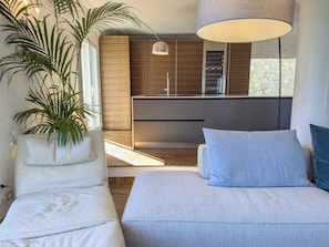 Une chambre moderne avec un canapé, un lit, une grande plante en pot et, au fond, un coin cuisine.
