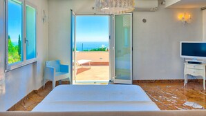 A bedroom with a bed, a TV, a chair, and a balcony with a view of the sea. - Villa Emanuele Costarainera: wonderful modern villa, for 16 ppl, with garden, heated pool, hot-tub (Costarainera)