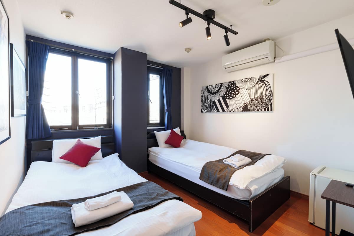 A hotel room with two beds, a desk, and an air conditioning unit.
