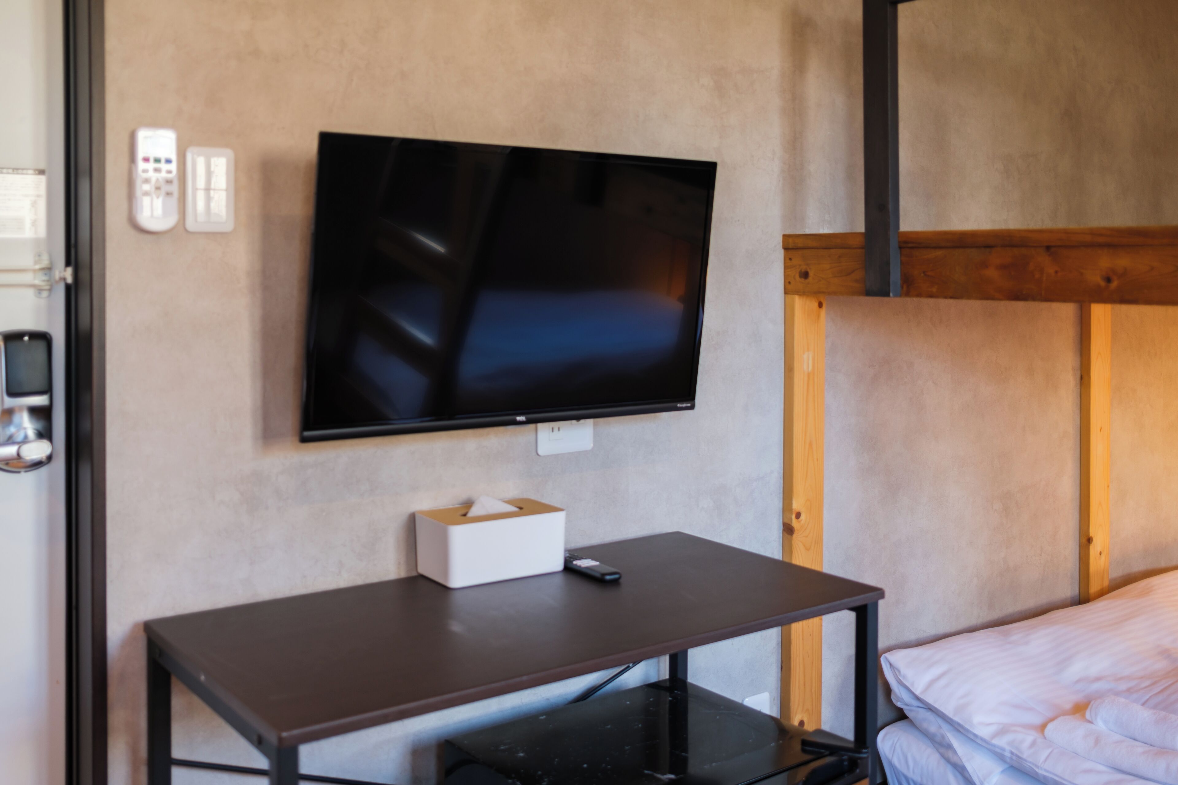 A room with a bed, a desk, a television mounted on the wall, and a telephone.