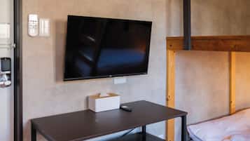 A room with a bed, a desk, a television mounted on the wall, and a telephone.