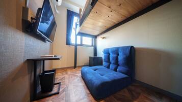A compact room with a wooden ceiling, a blue sofa, a TV on a stand, and a small table.