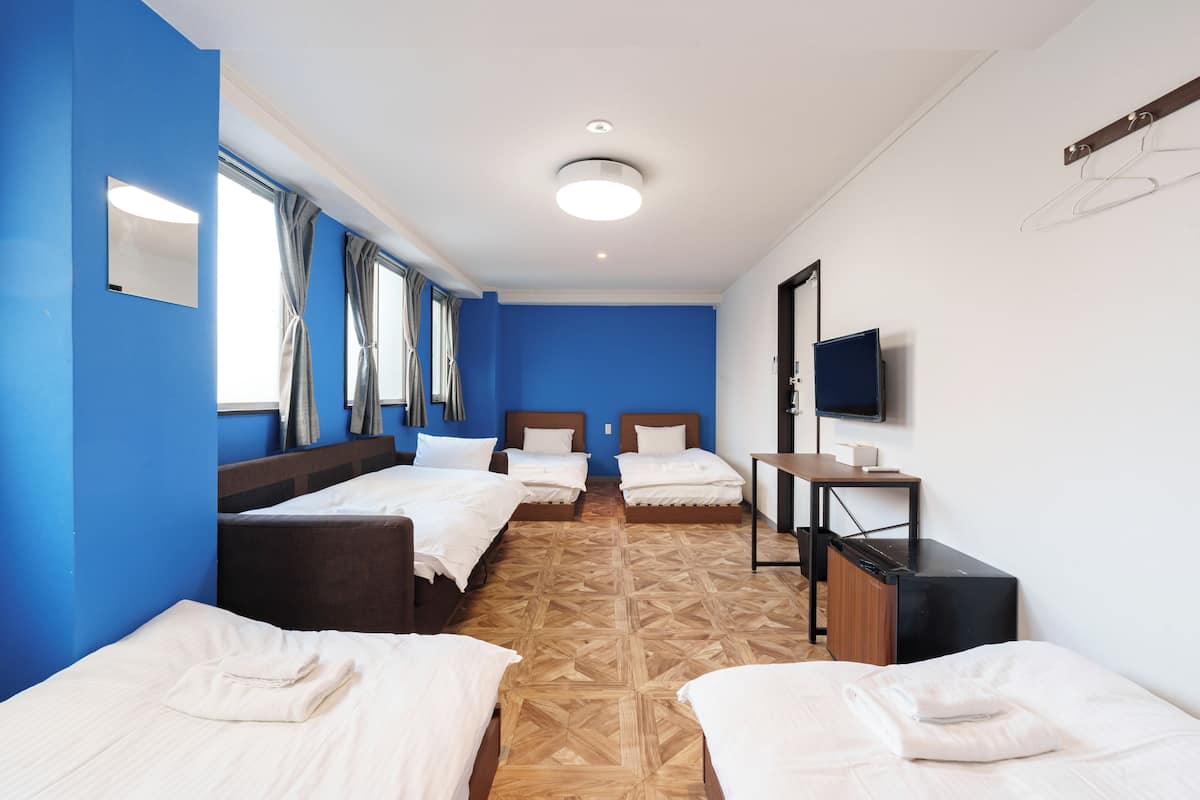 A hotel room with two single beds, a desk, a TV, and a window with curtains.