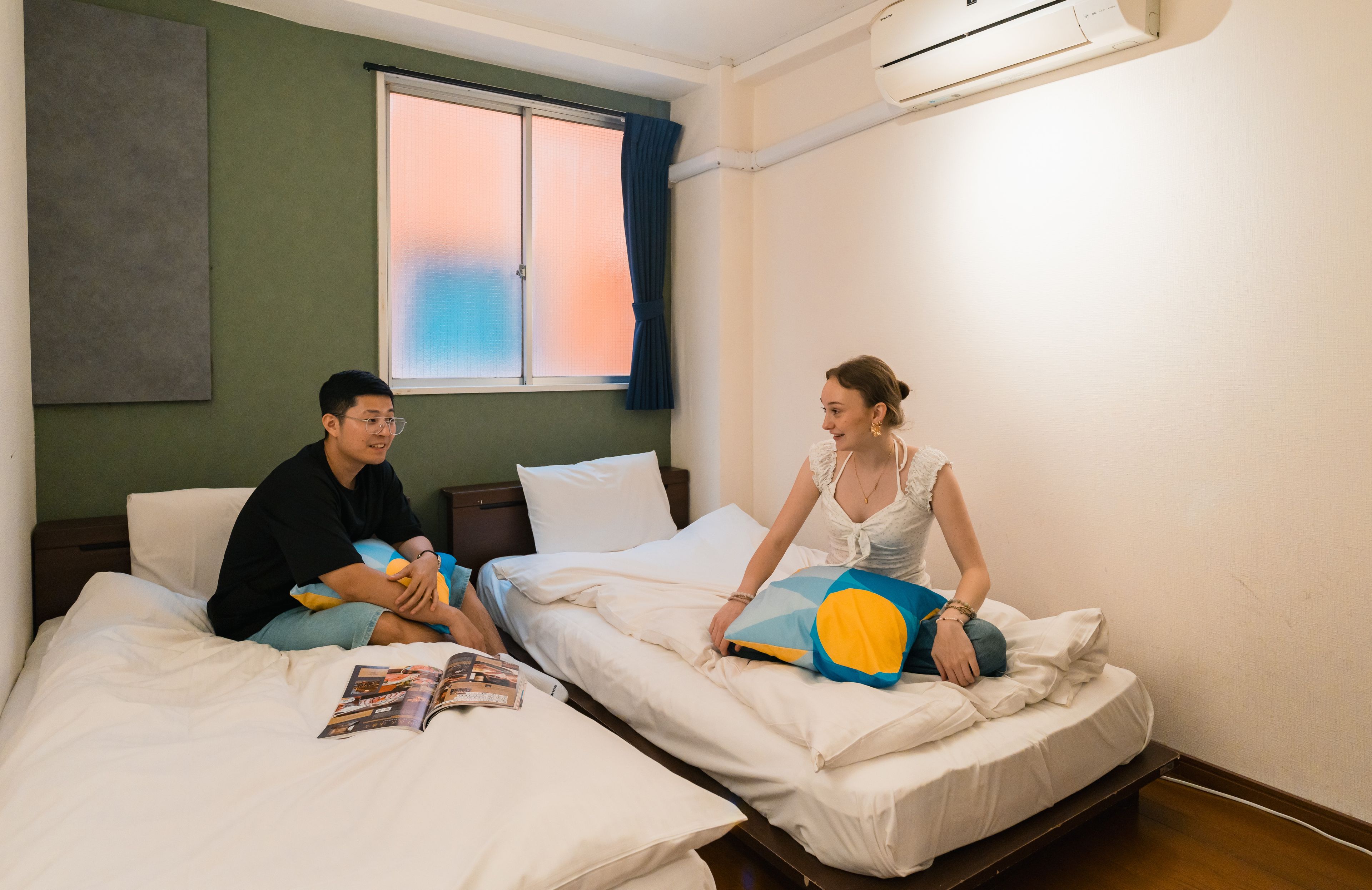 A hotel room with two beds, a window with curtains, and an air conditioning unit.