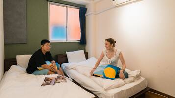A hotel room with two beds, a window with curtains, and an air conditioning unit.