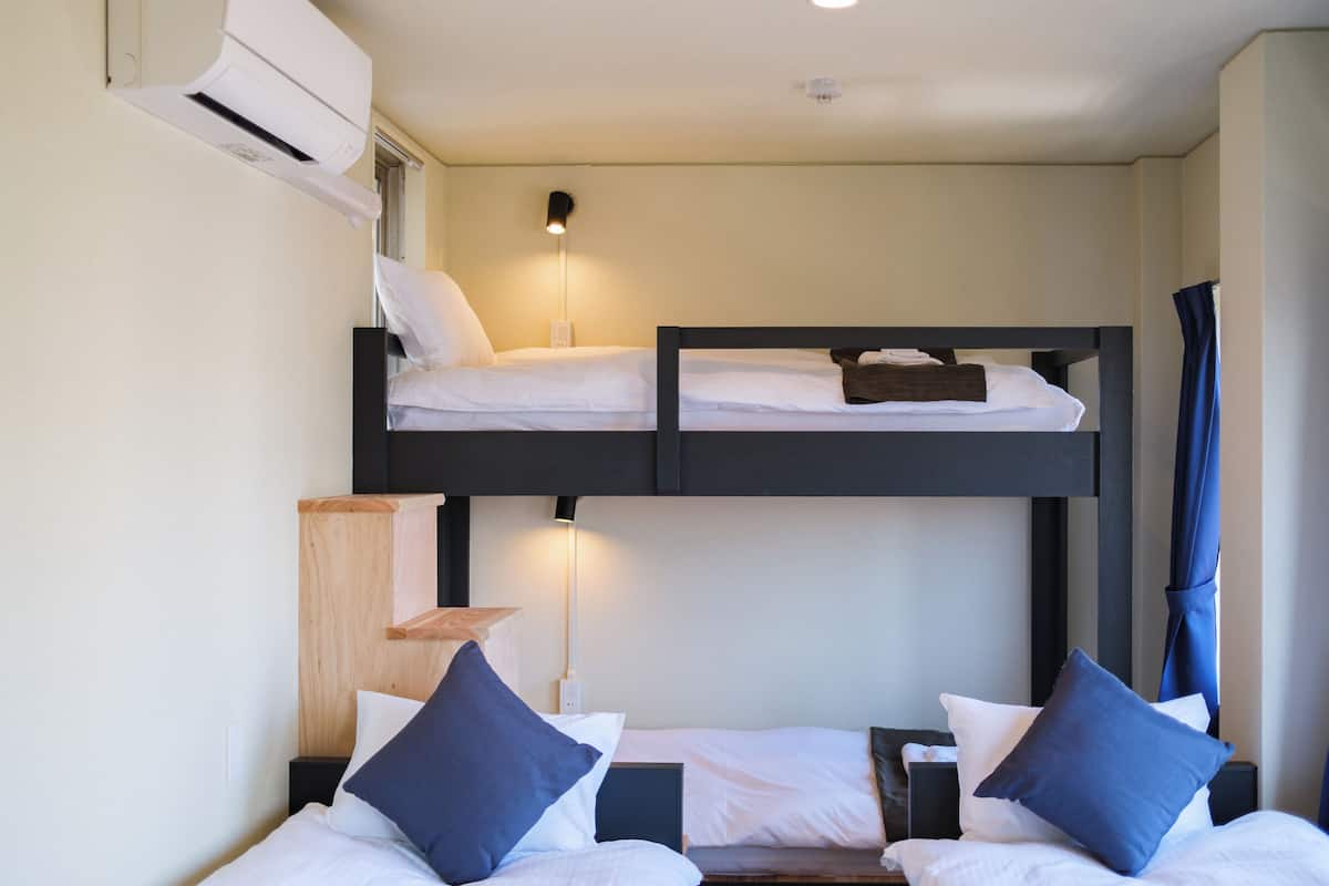 A bunk bed room with two beds, a bedside table, a lamp, and an air conditioning unit.