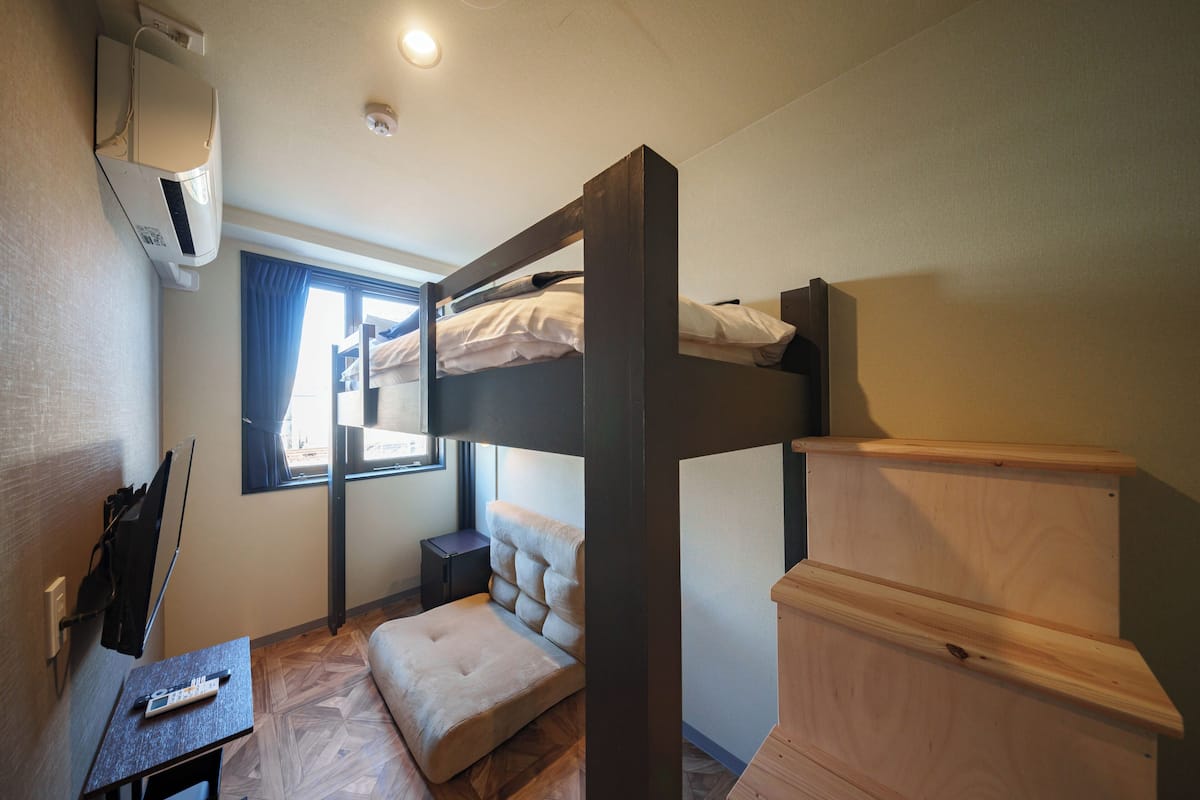 A bunk bed room with a small desk, a window with curtains, and a wall-mounted air conditioner.