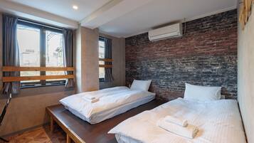 A hotel room with two beds, a bench, a brick wall, and an air conditioning unit.