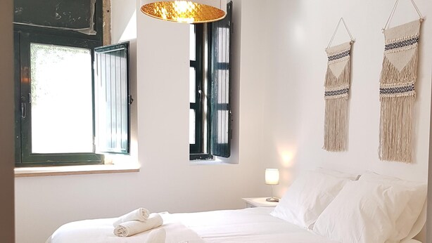 A bedroom with a bed, a hanging light fixture, a window with blinds, and wall decorations. - Central and Modern Apartment in a Restored Chalet (Sintra)