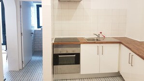 A kitchen with white cabinets, a stainless steel oven, a sink with a red faucet, and a window above the sink. - Central and Modern Apartment in a Restored Chalet (Sintra)