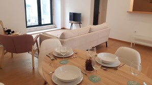 A dining area with a wooden table set for four, a white sofa, and a TV on a stand. - Central and Modern Apartment in a Restored Chalet (Sintra)