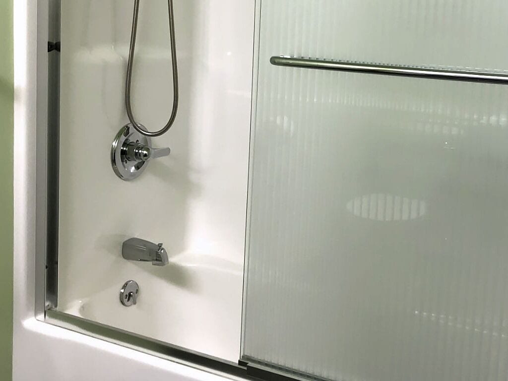 Une douche avec une porte en verre, un robinet et une molette de réglage.
