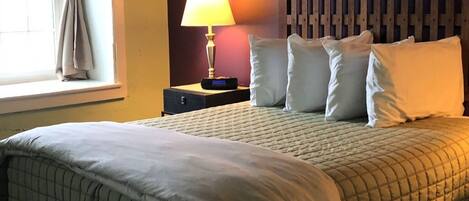 Una cama bien hecha con un cubrecolchón acolchado, una lámpara de noche y un cabecero de madera.