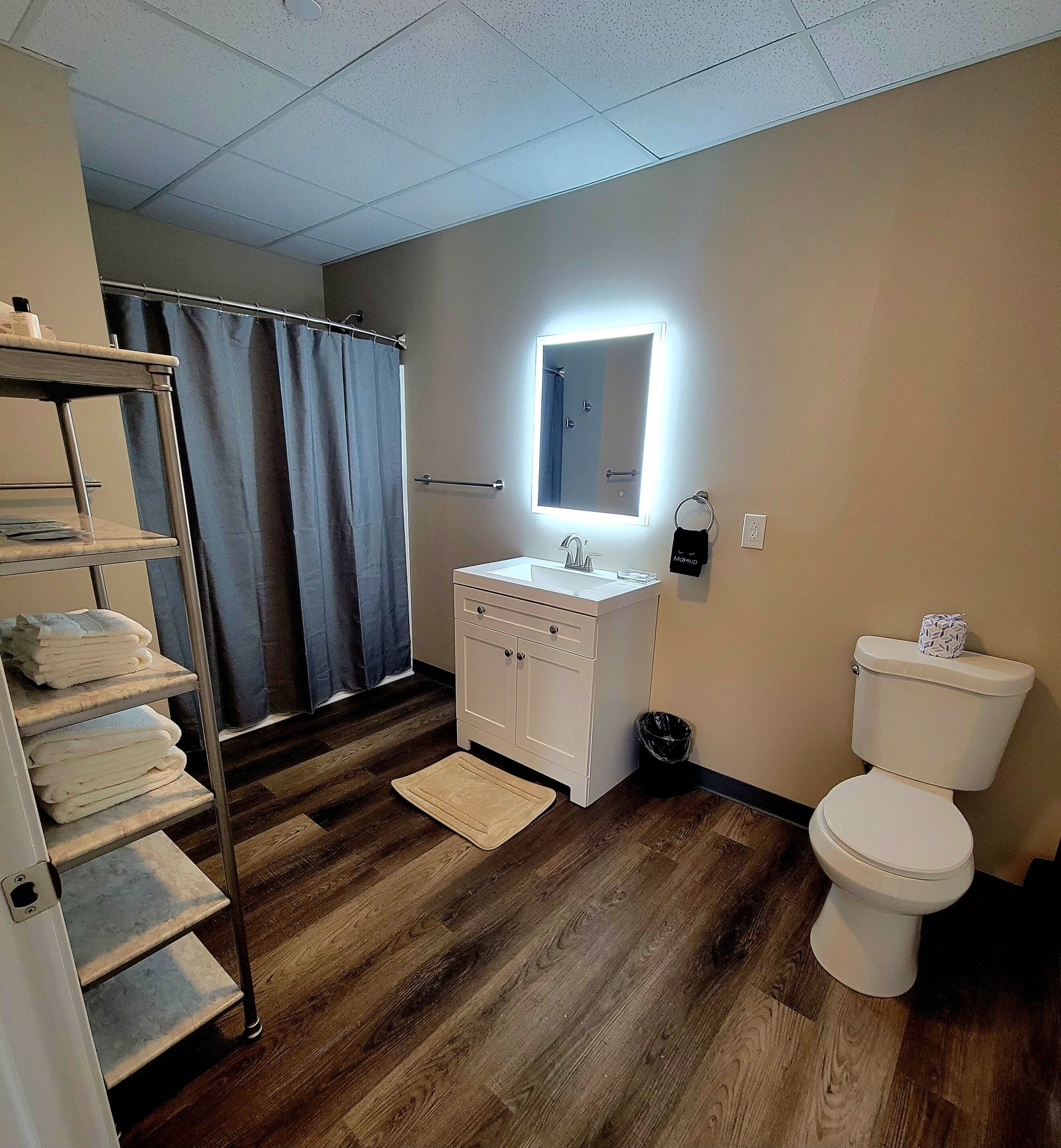 A bathroom with a wooden floor, a white sink, a mirror, a towel rack, and a toilet.