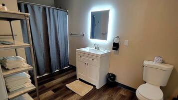 A bathroom with a wooden floor, a white sink, a mirror, a towel rack, and a toilet.