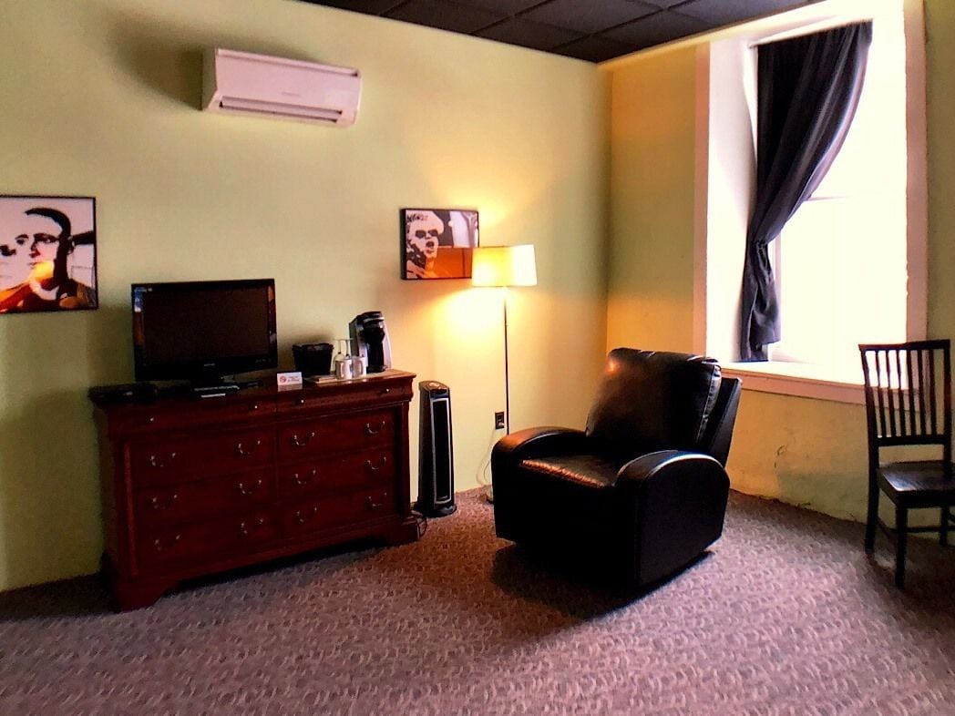 A room with a TV, a dresser, a chair, a lamp, and a window with curtains.