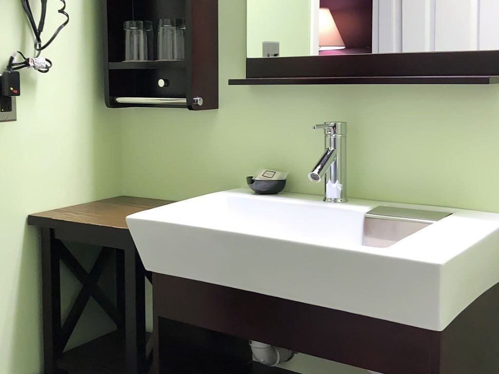 A bathroom with a white sink, a mirror above it, and a small shelf with toiletries.
