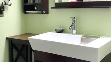A bathroom with a white sink, a mirror above it, and a small shelf with toiletries.
