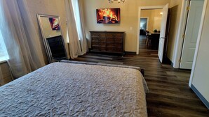 Een slaapkamer met een groot bed, een kaptafel, een schilderij van een vuur en een kroonluchter.