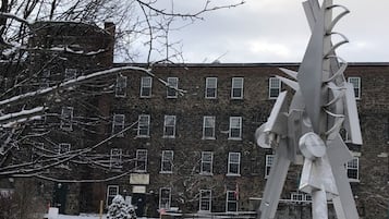 Un espacio exterior cubierto de nieve con una escultura de metal, un edificio de ladrillo y un pequeño árbol.