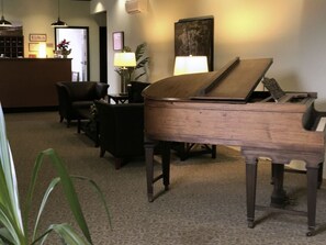 A grand piano in a lobby area with a reception desk, chairs, and a plant.