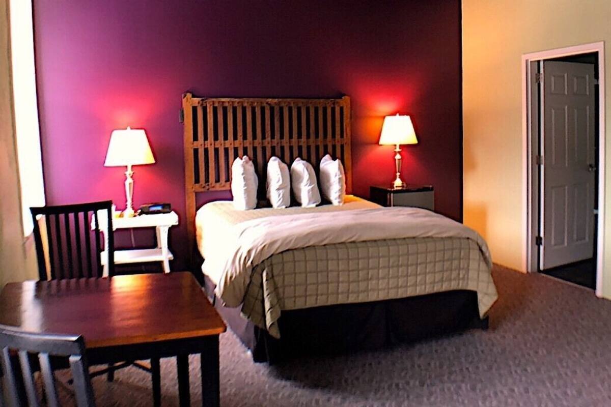 A hotel room with a bed, two bedside tables with lamps, a chair, and a door.