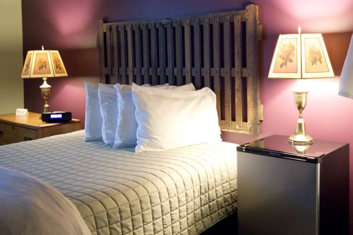 A neatly made bed with white linens, a bedside table with a lamp, and a radiator above the bed.