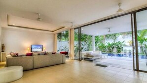 Una sala de estar moderna con un sofá, un televisor y una puerta de vidrio que da a una zona de piscina.